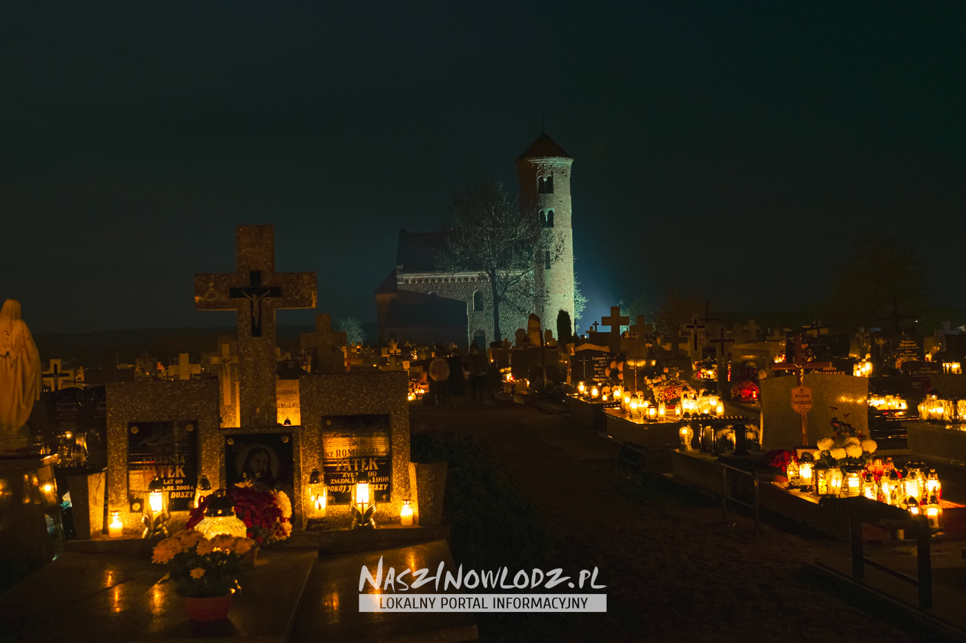 Groby i płonące znicze na cmentarzu w Inowłodzu z kościołem św. Idziego w tle
