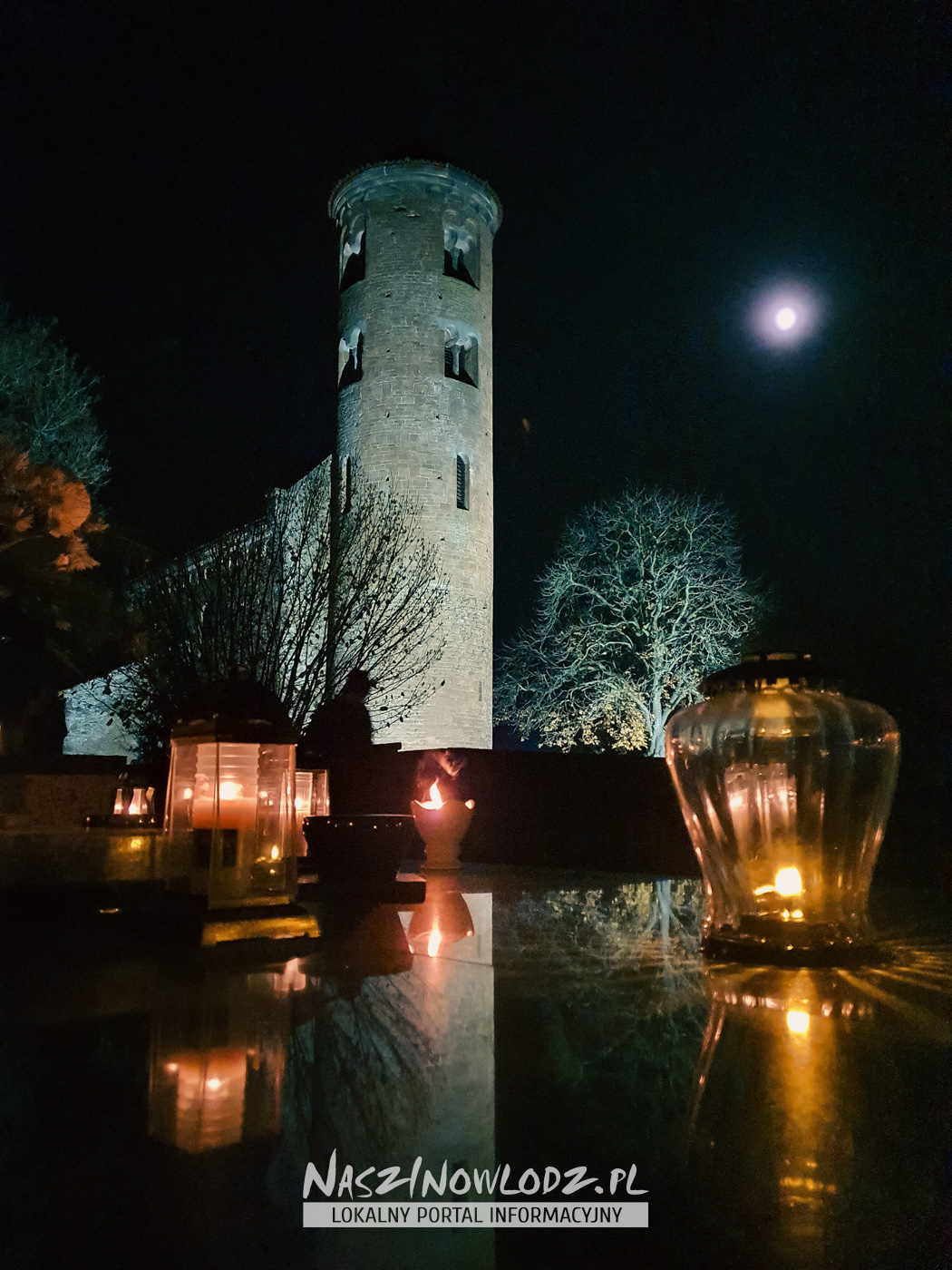 Płonące znicze na pierwszym planie i oświetlona wieża kościoła św. Idziego nocą